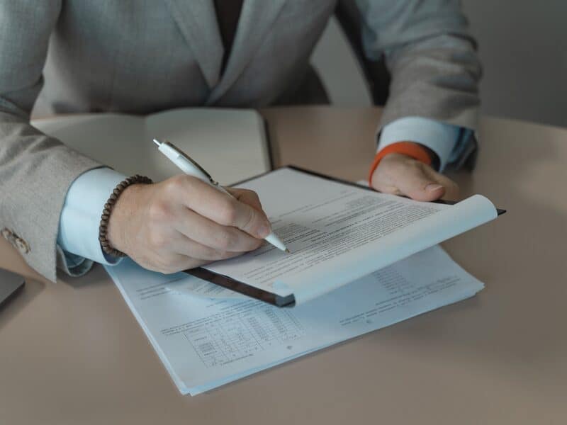 A person in a suit reviewing and signing a document on a clipboard.